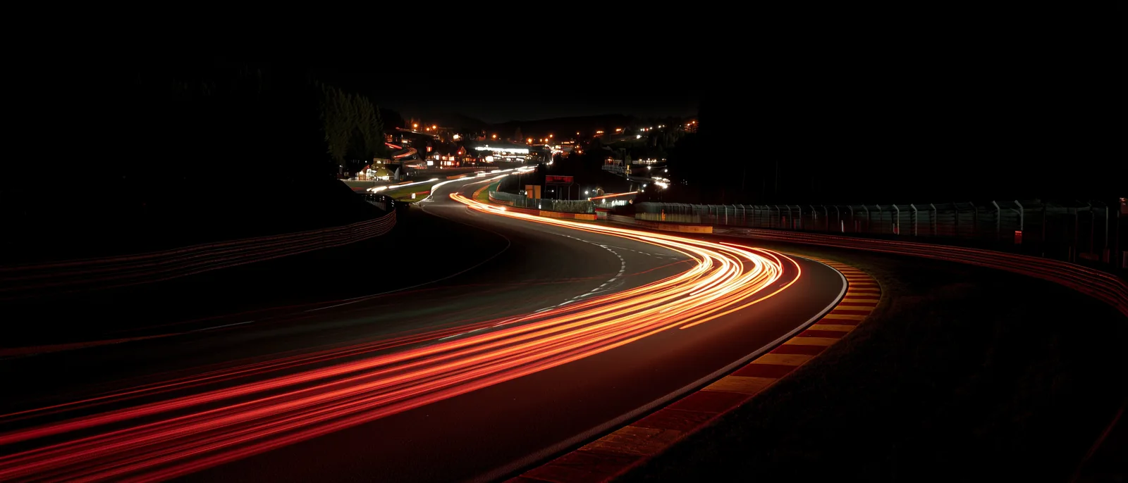 Eau Rouge corner at Spa-Francorchamps at night, red taillights streaking up the hill